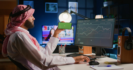 man-holding-phone-while-analyzing-data-on-computer