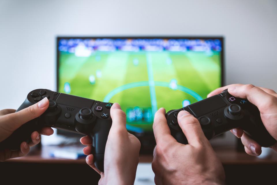 two-people-holding-video-game-controllers-with-sports-video-game-on-tv