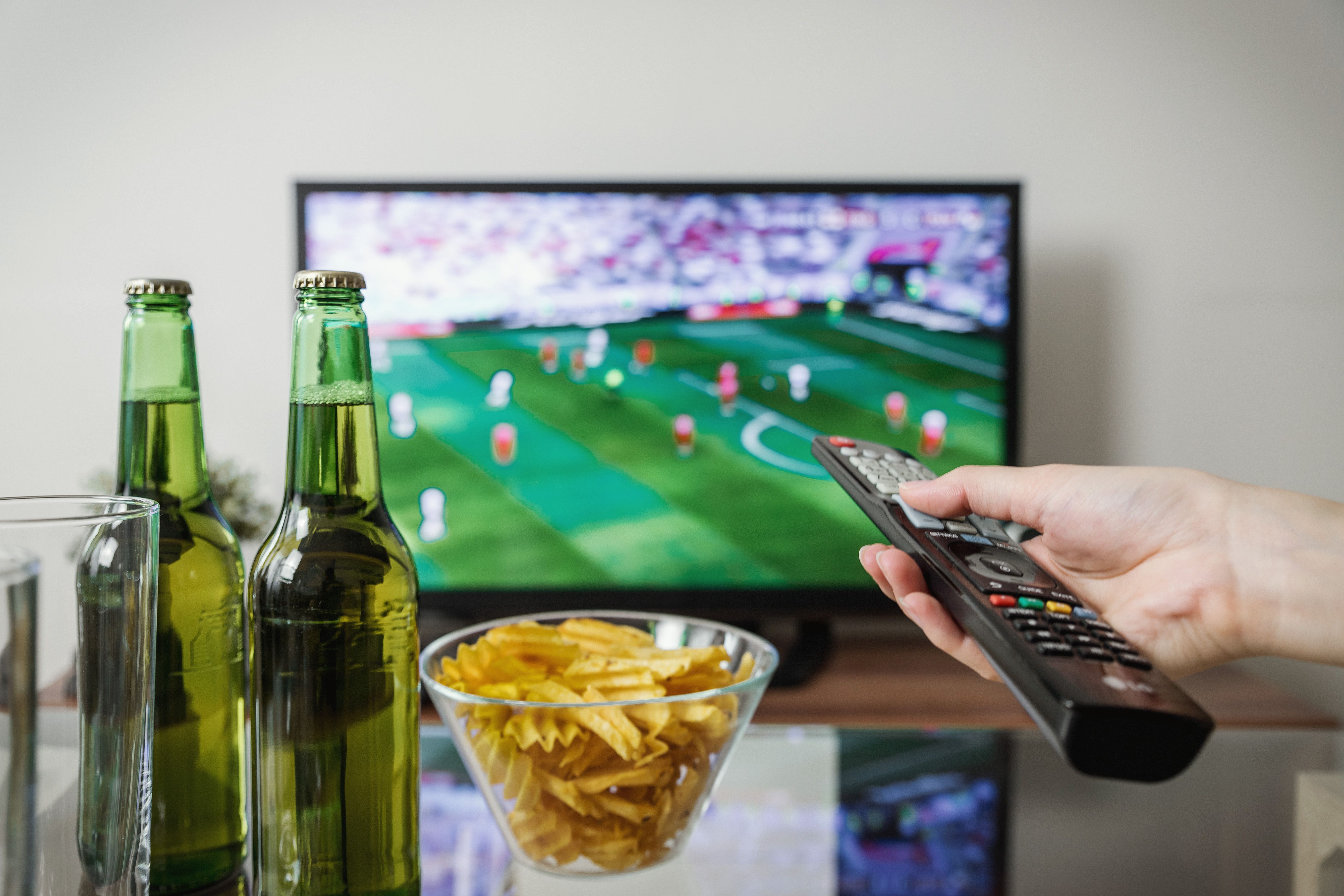 soccer-fan-watching-game-with-remote-sparkling-water-glass-bottles-and-chips
